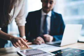 two people behind desk using ipad and computer to calculate investment numbers.